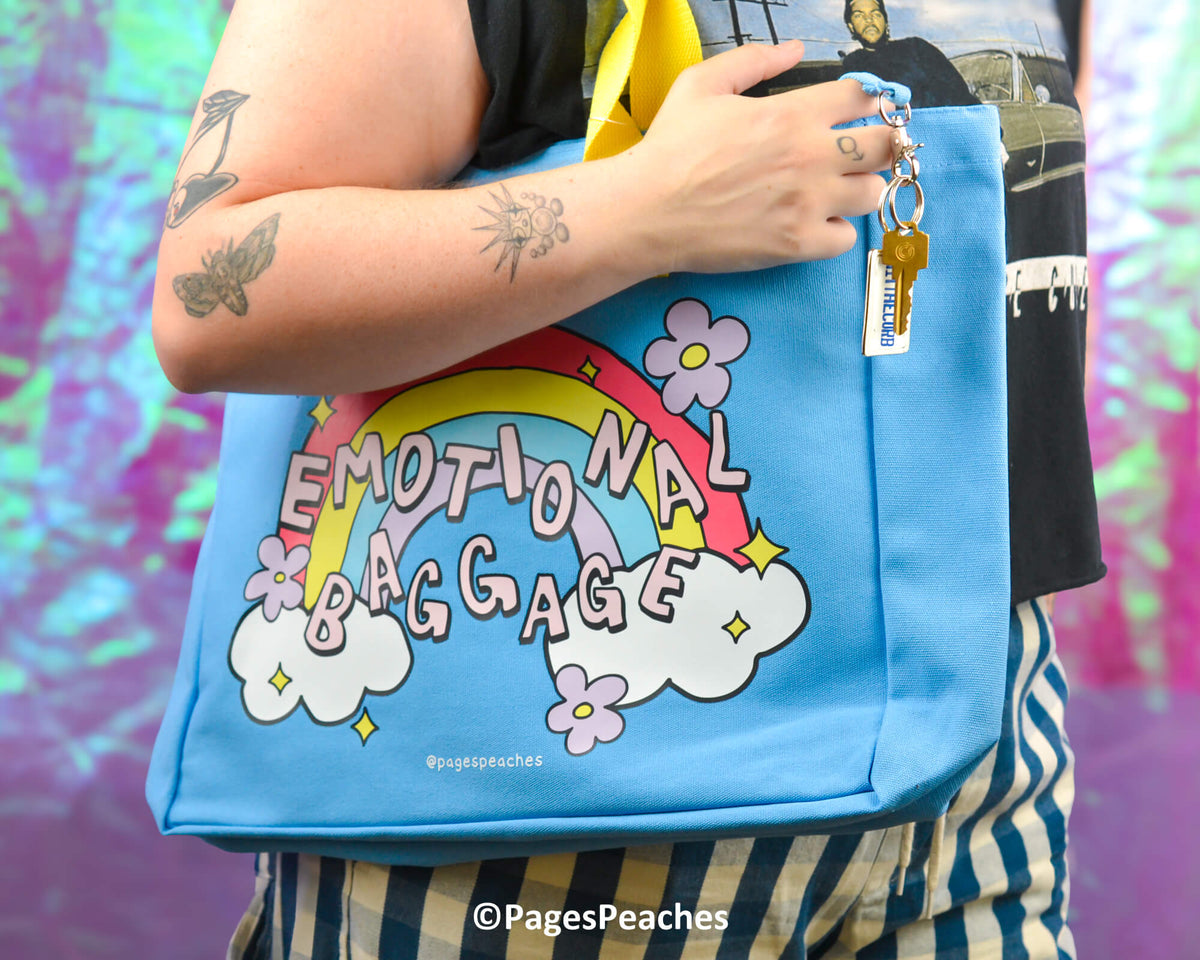 Blue bag with 'Emotional Baggage' design held by a person against a colorful background
