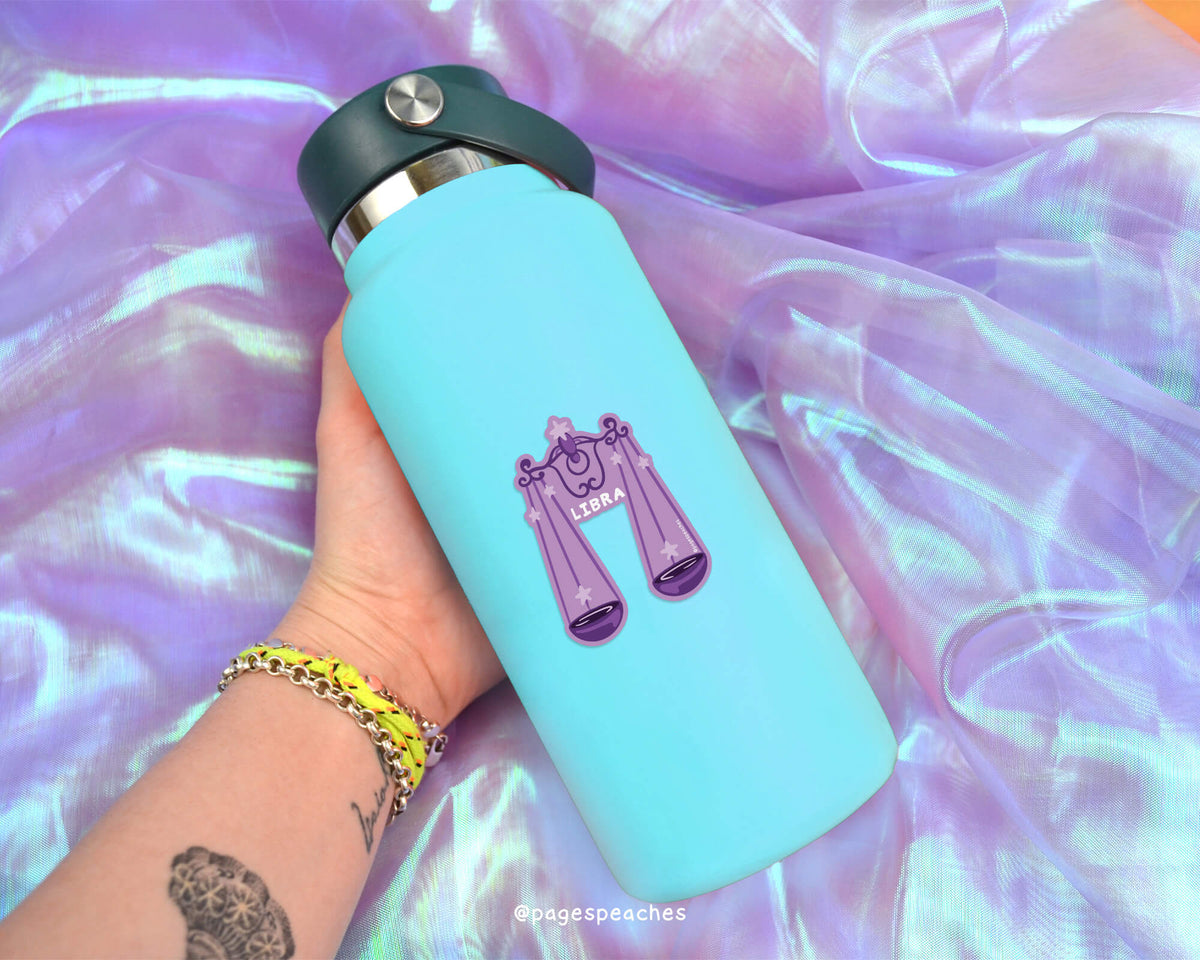 A person's hand holding a blue water bottle with a purple and white design on it, against a purple and blue fabric background.
