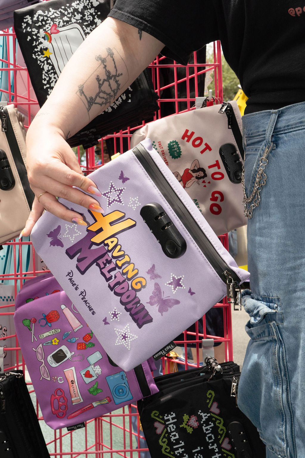 A person is holding a purple bag with a colorful design, surrounded by other bags and accessories in a store setting.