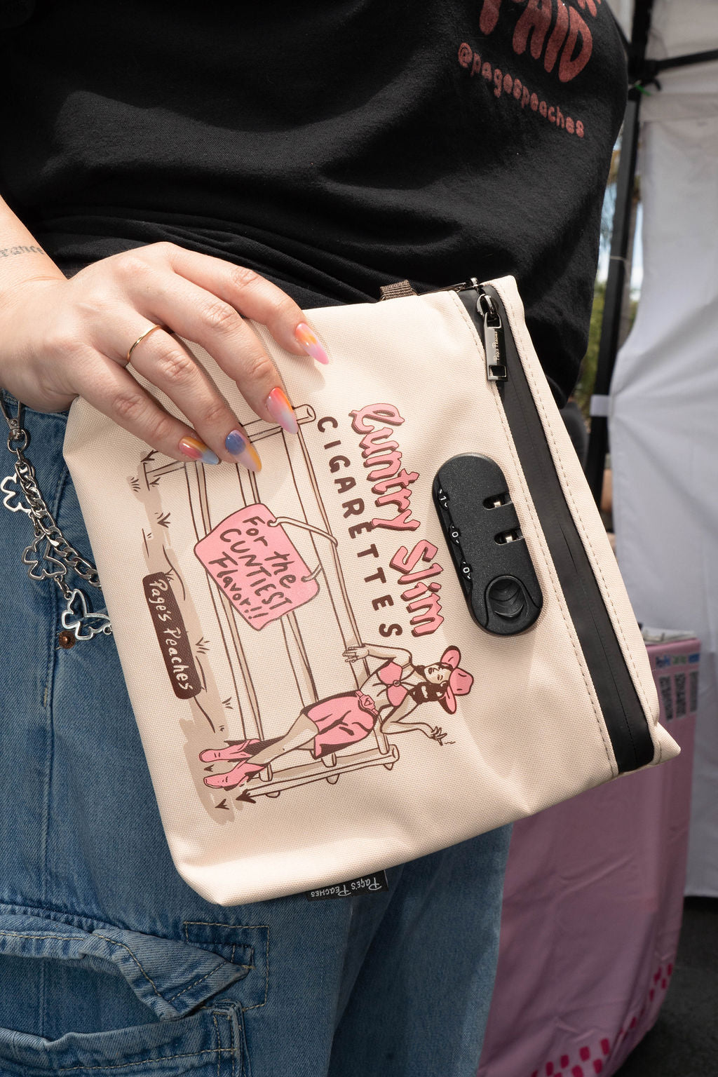 A person is holding a white bag with a cartoon character on it, wearing a black shirt with text on it.
