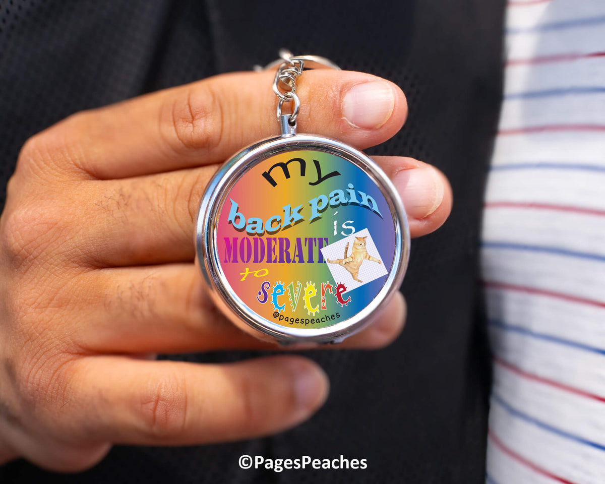 A person is holding a colorful keychain with the text "MY back pain is moderate to severe" printed on it.