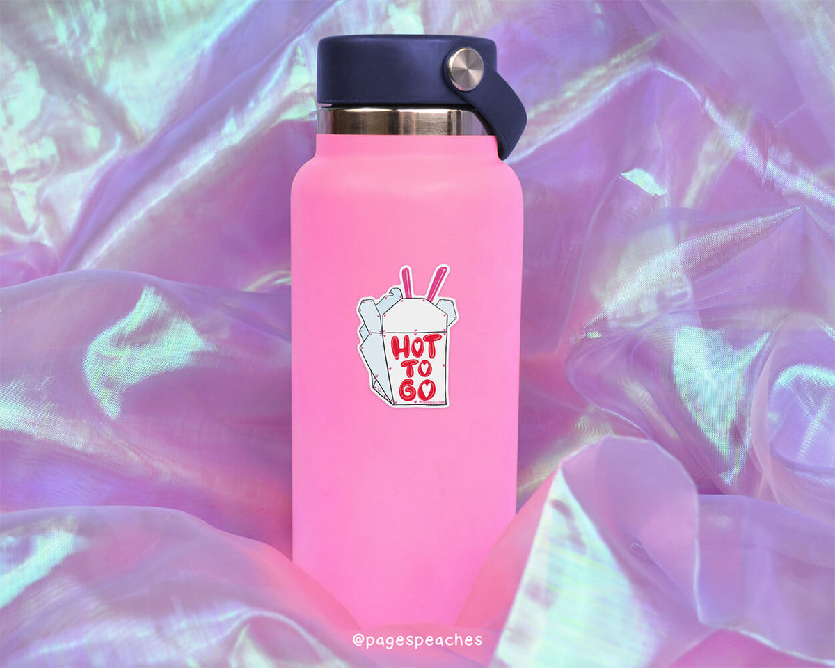 A pink water bottle with a sticker that says "HOT TO GO" is placed on a purple fabric background.