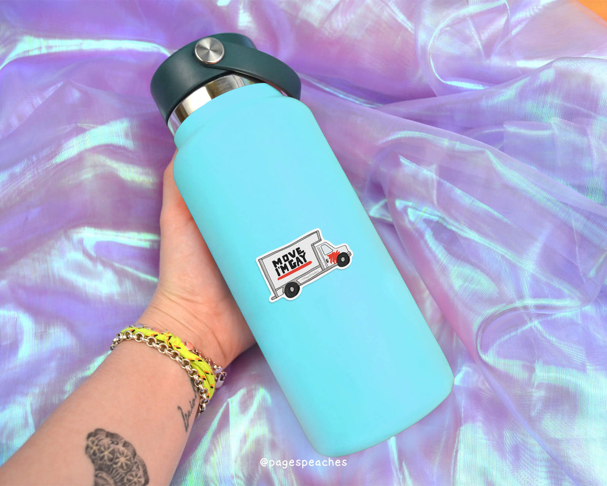 A person's hand holding a blue water bottle with a sticker of a truck on it, against a purple fabric background.