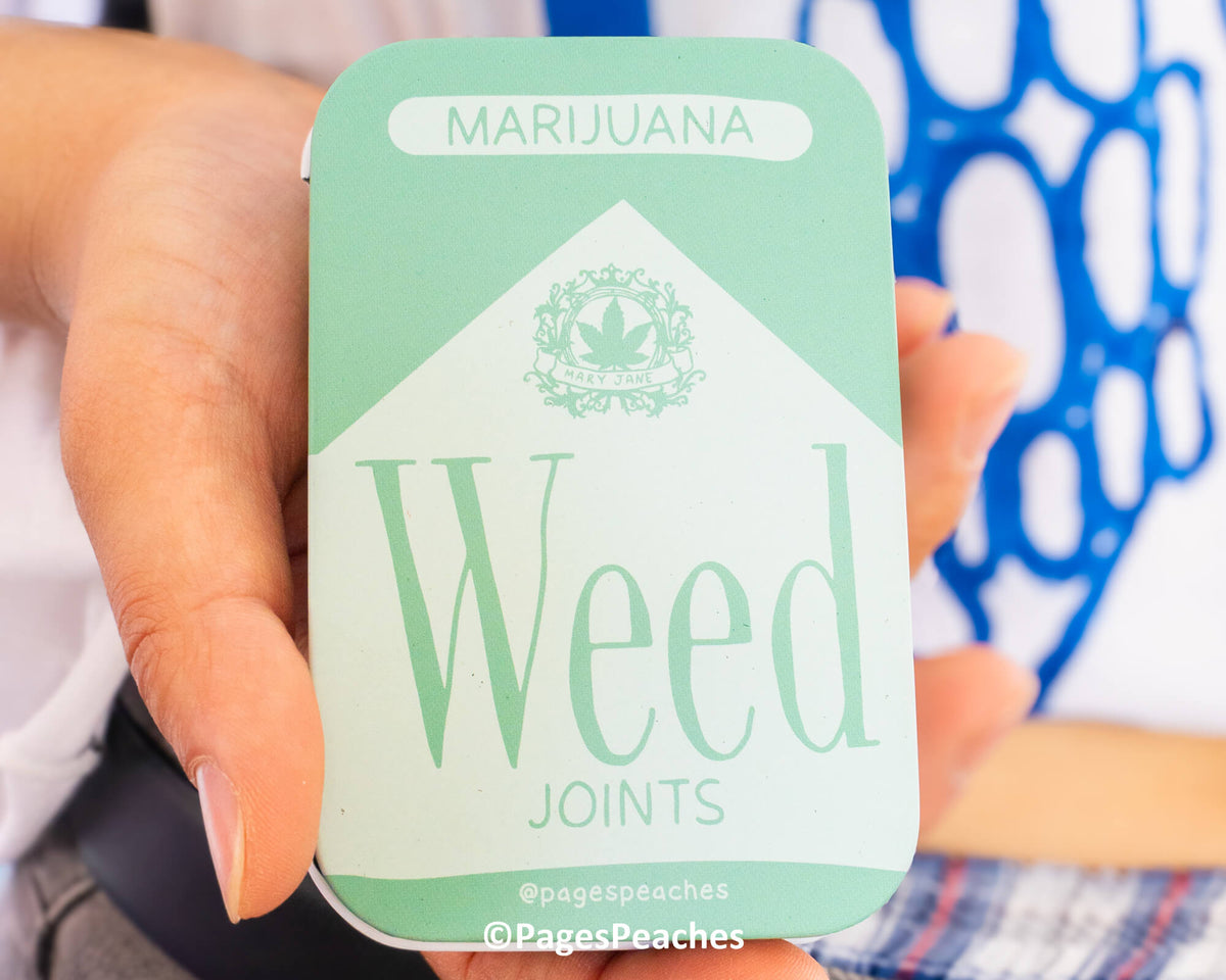 A person is holding a mint-colored box with the word "Marijuana" written on it, and the word "Weed" below it.