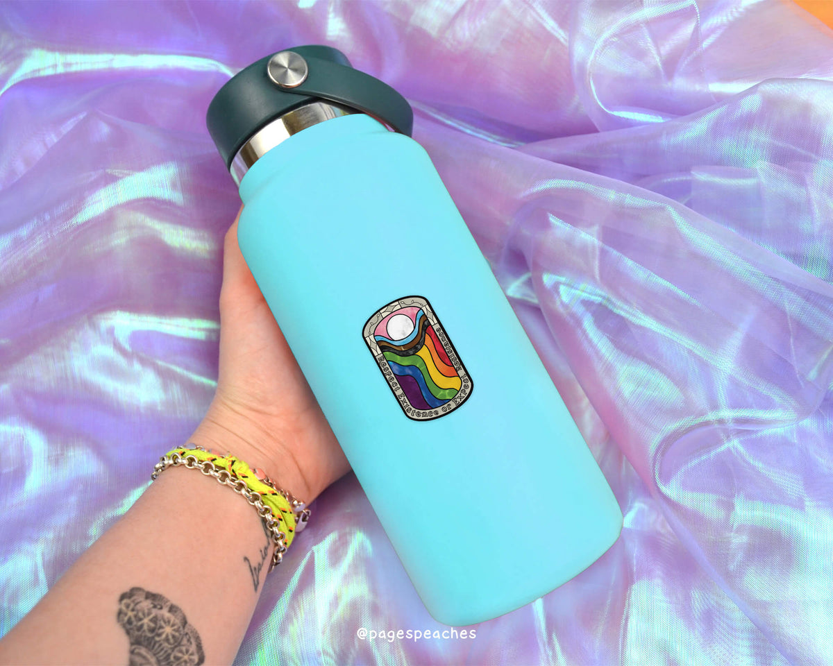 A person's hand holding a blue water bottle with a colorful sticker on it, against a purple fabric background.