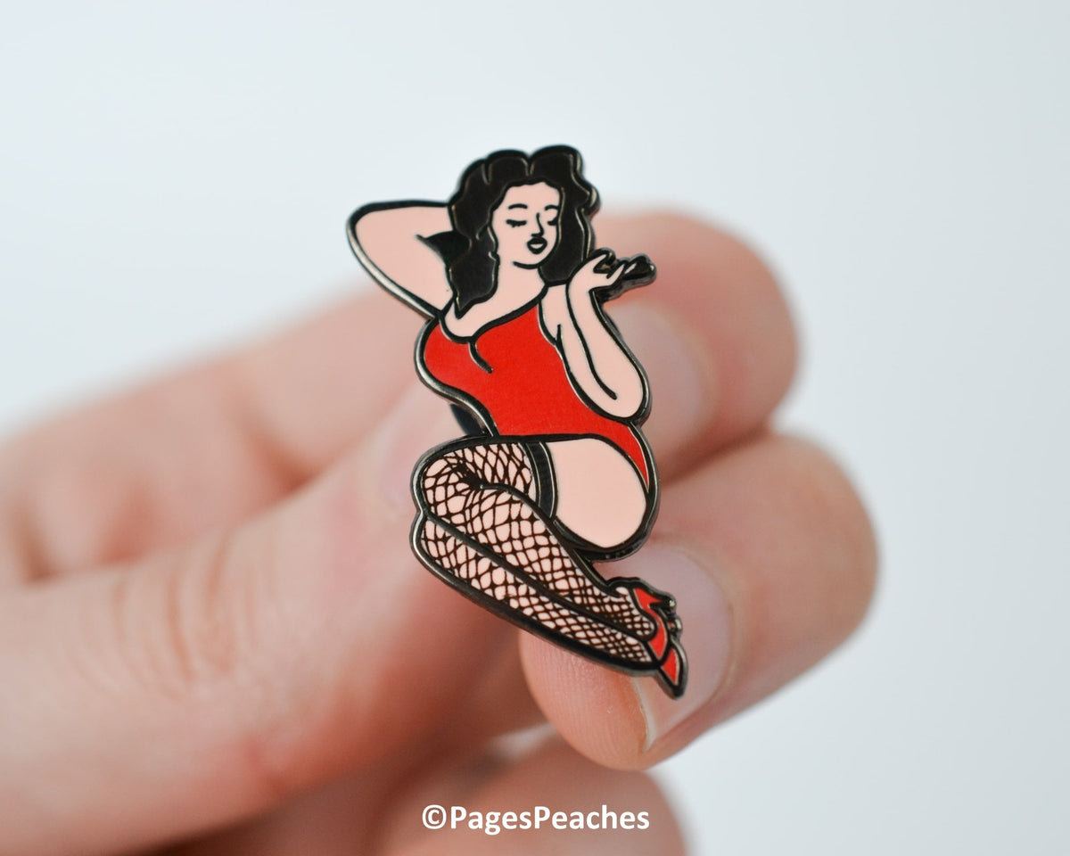 Close-up of a hand holding a curvy pinup enamel pin in a red bodysuit and fishnet stockings.