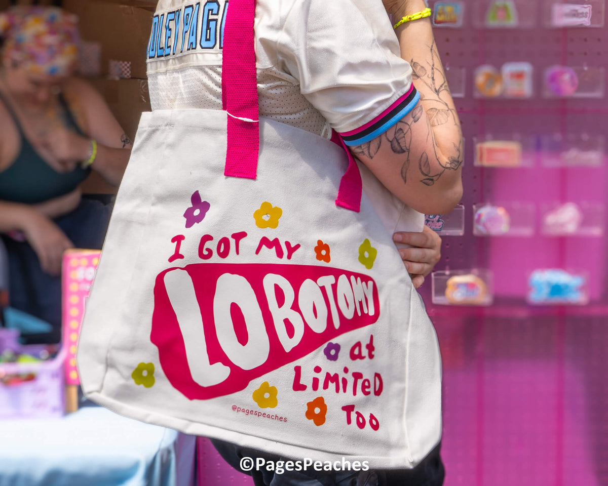 A person is holding a white tote bag with colorful text and flower designs printed on it.