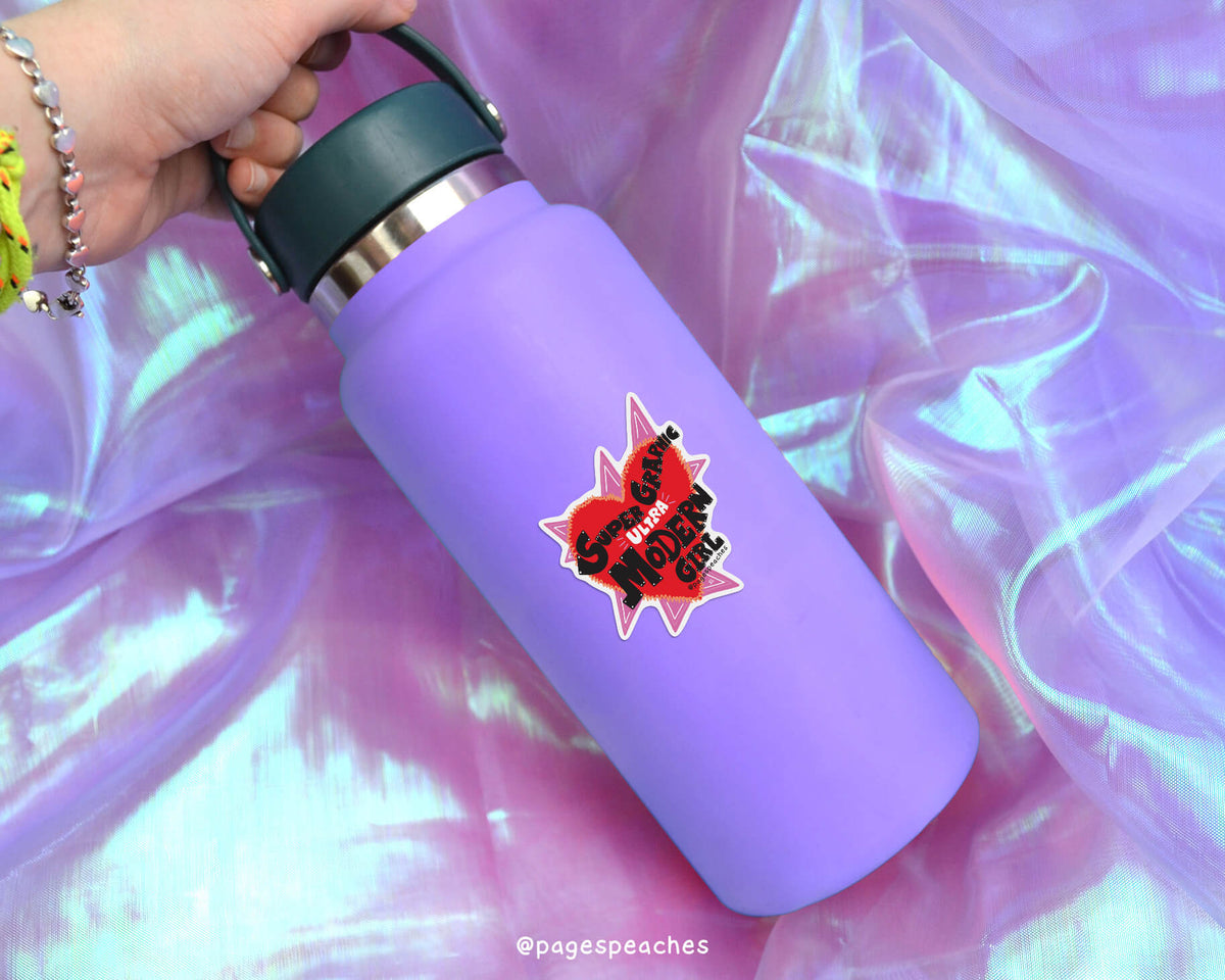 A purple water bottle with a red and black sticker on it, held in a hand against a purple fabric background.