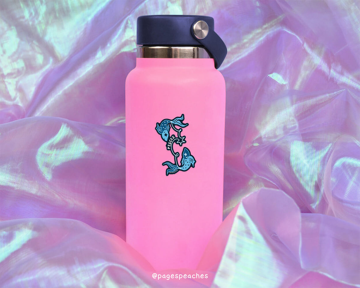 A pink water bottle with a blue fish design on it, placed on a purple fabric background.