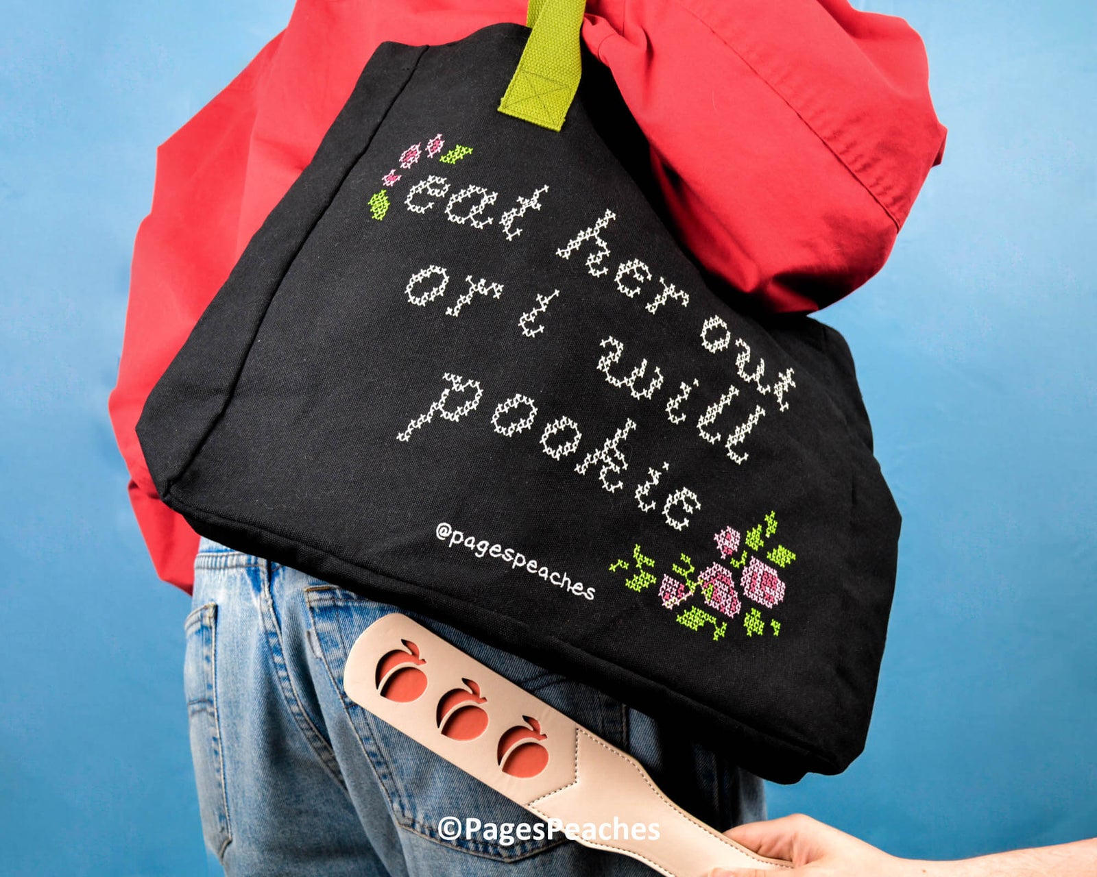 Black canvas tote bag with green straps and stitched-style text reading “Eat her out or I will pookie,” decorated with pink and purple pixel flowers