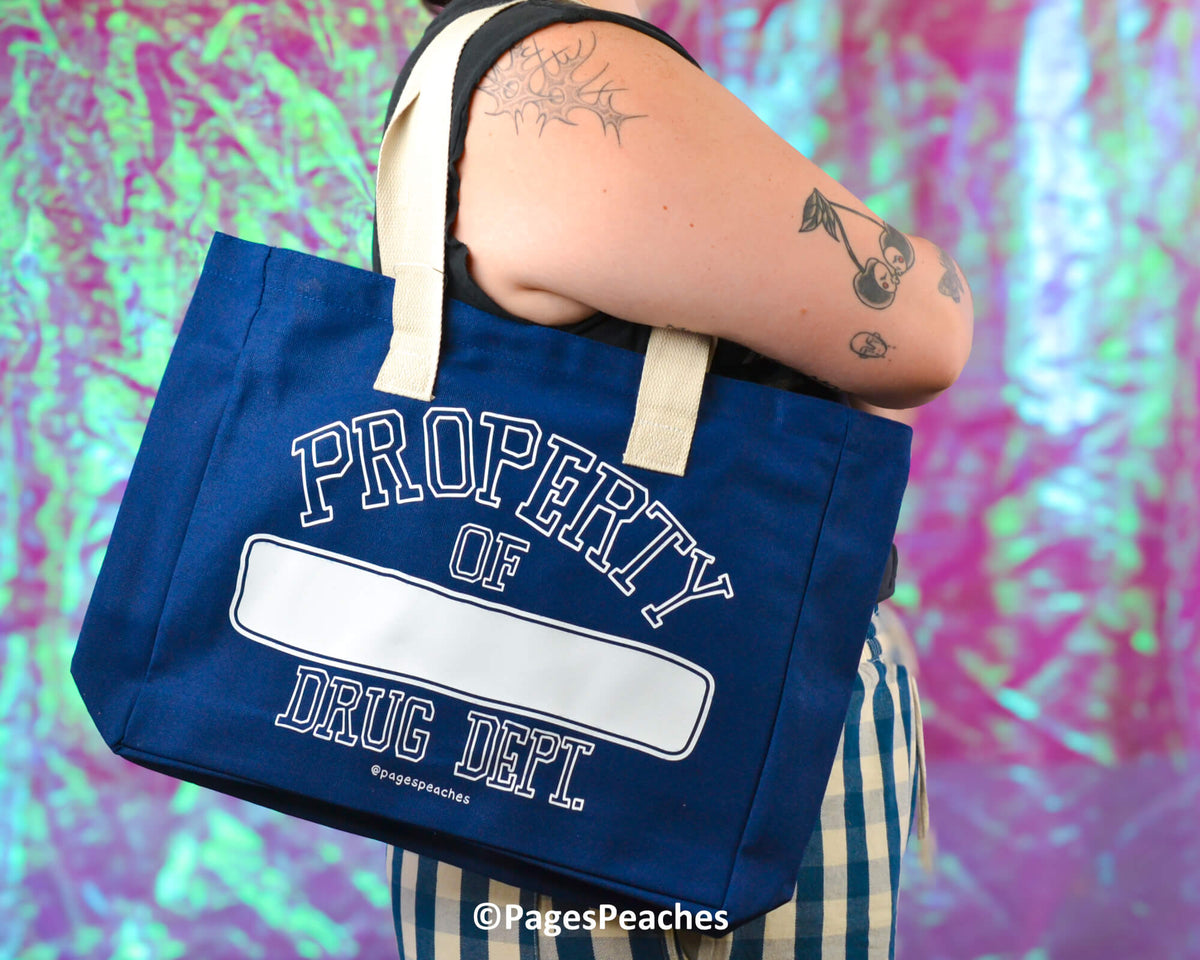 Person holding a blue tote bag with 'Property of Drug Dept' text against a colorful background
