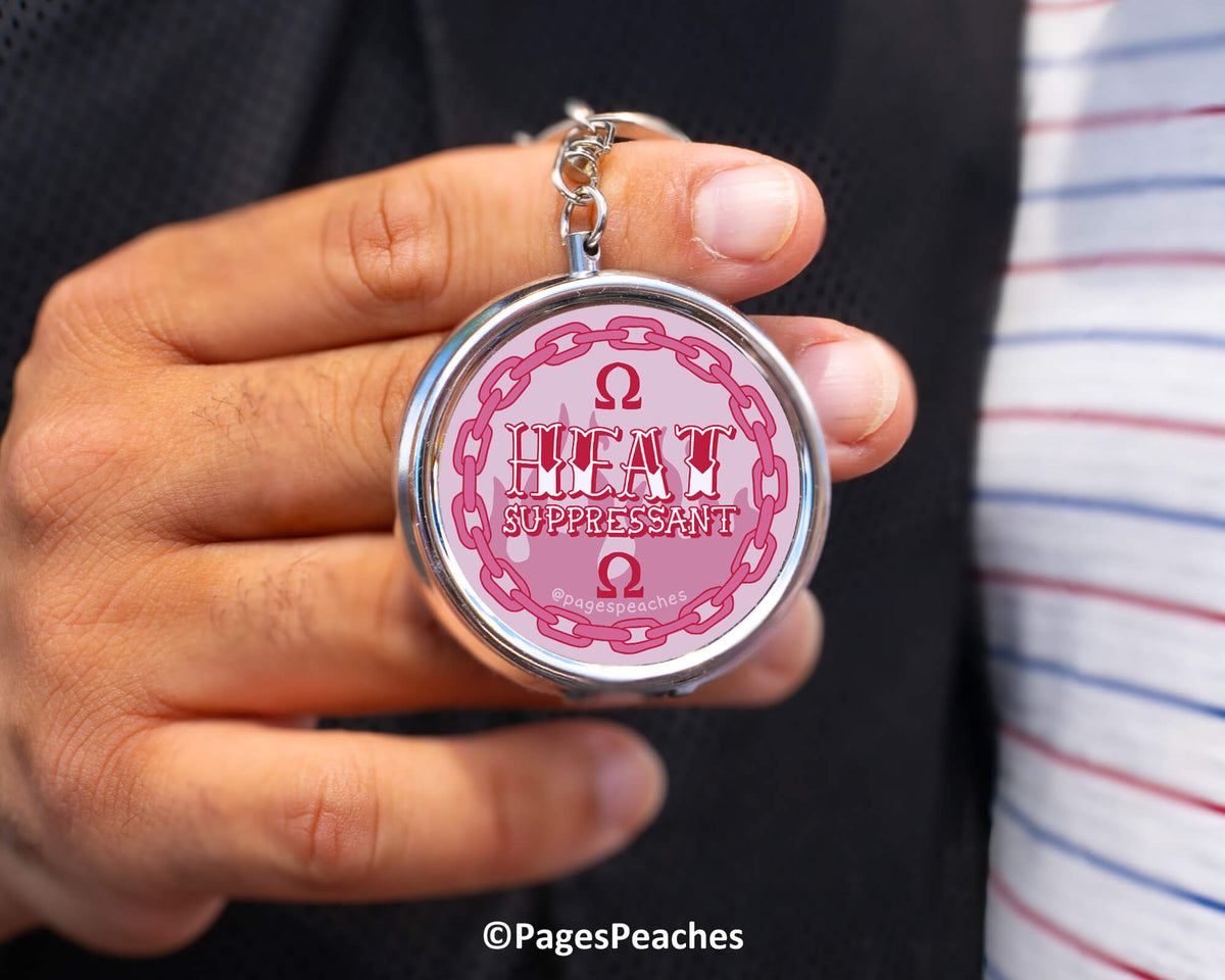 A person is holding a keychain with a circular design featuring the text "HEAT SUPPRESSANT" and an Omega symbol.