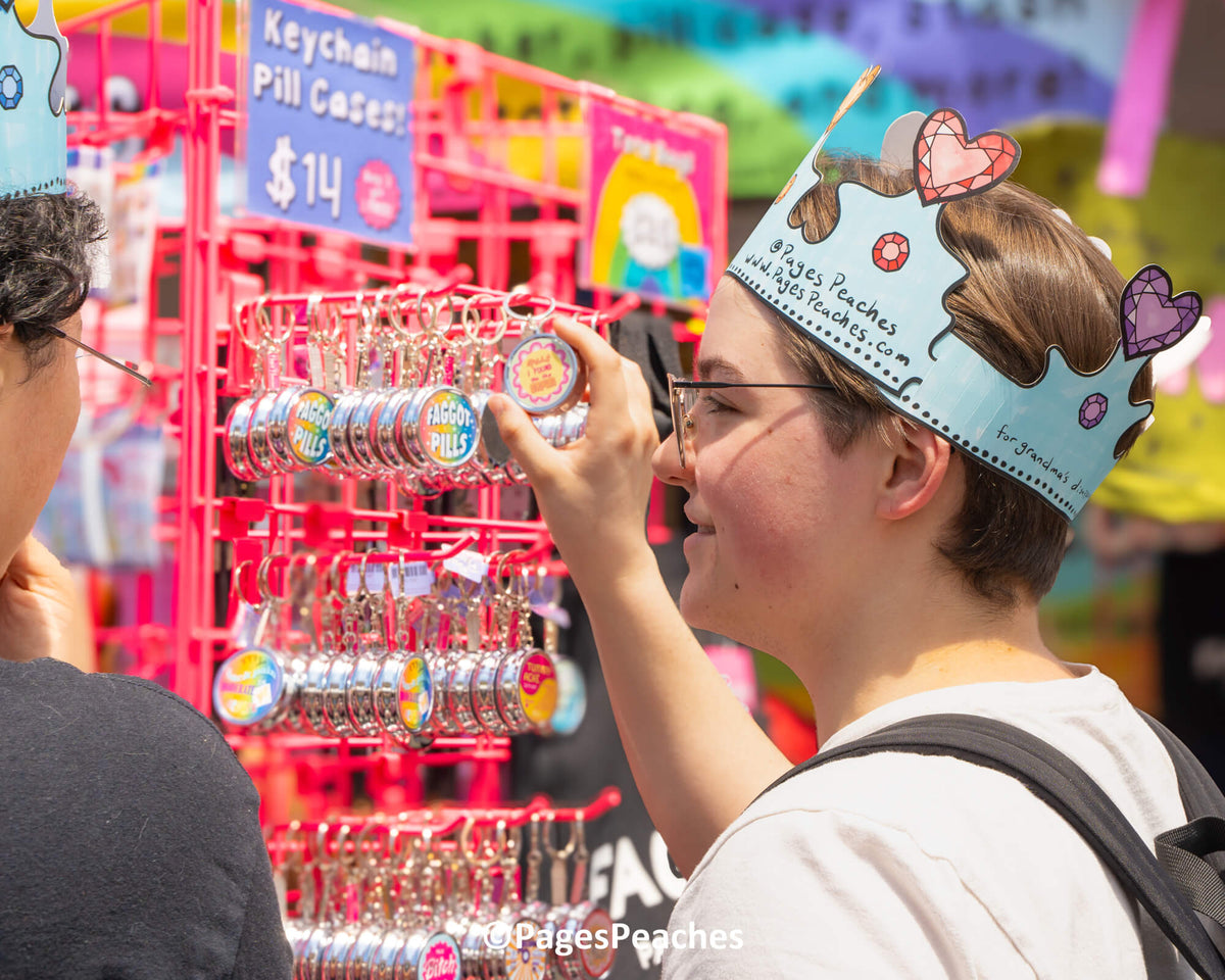 A person wearing a crown and glasses is examining a keychain on a display rack, surrounded by other keychains and items.