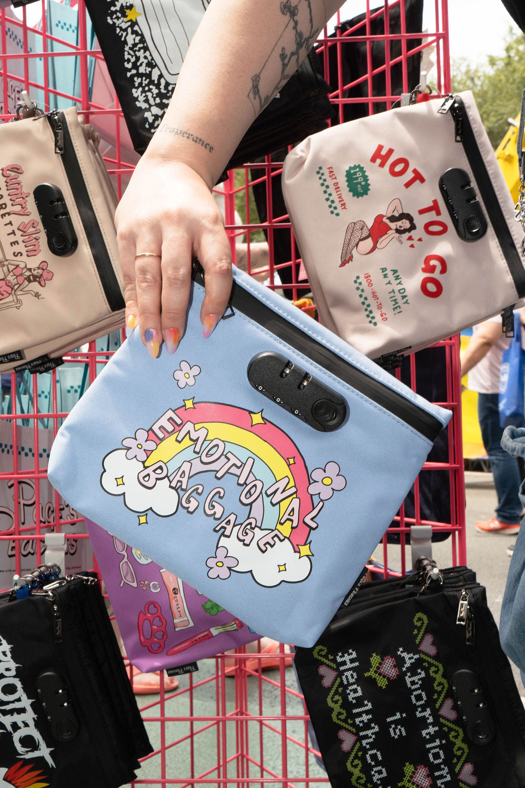 A person's hand holding a colorful bag with a rainbow design and the text "emotional baggage" printed on it.