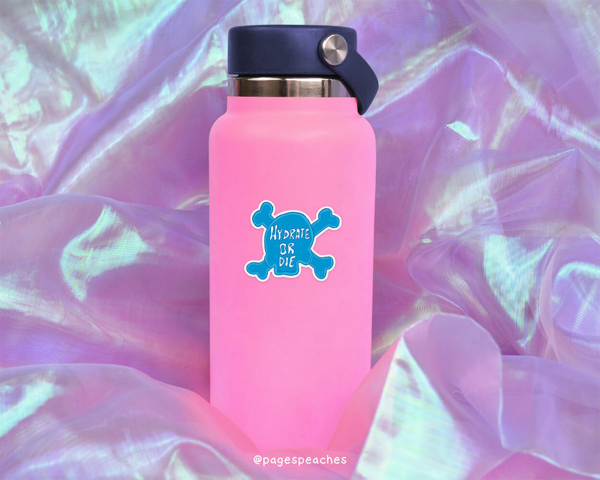 A pink water bottle with a blue skull sticker on it, placed on a purple fabric background.