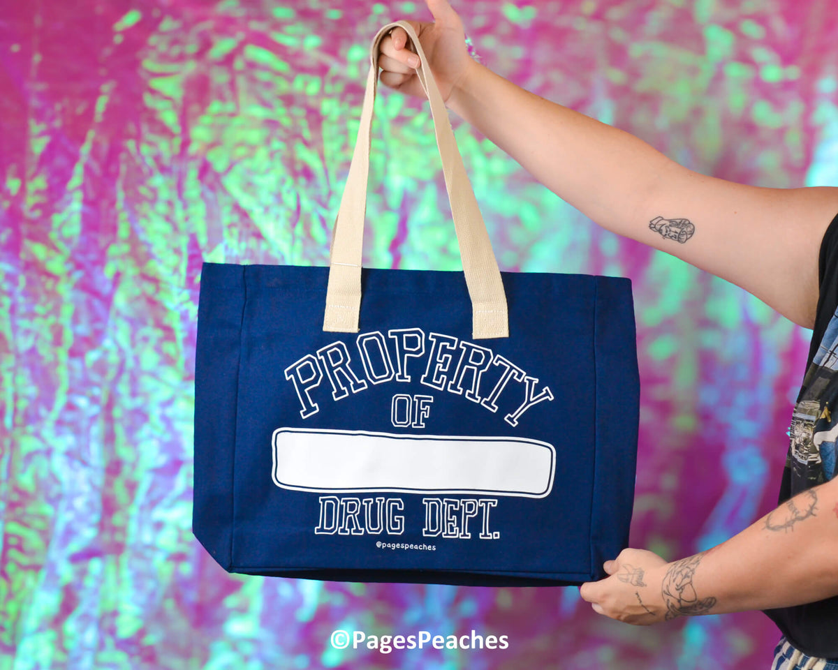 Person holding a blue tote bag with 'Property of Drug Dept' text against a colorful, abstract background.