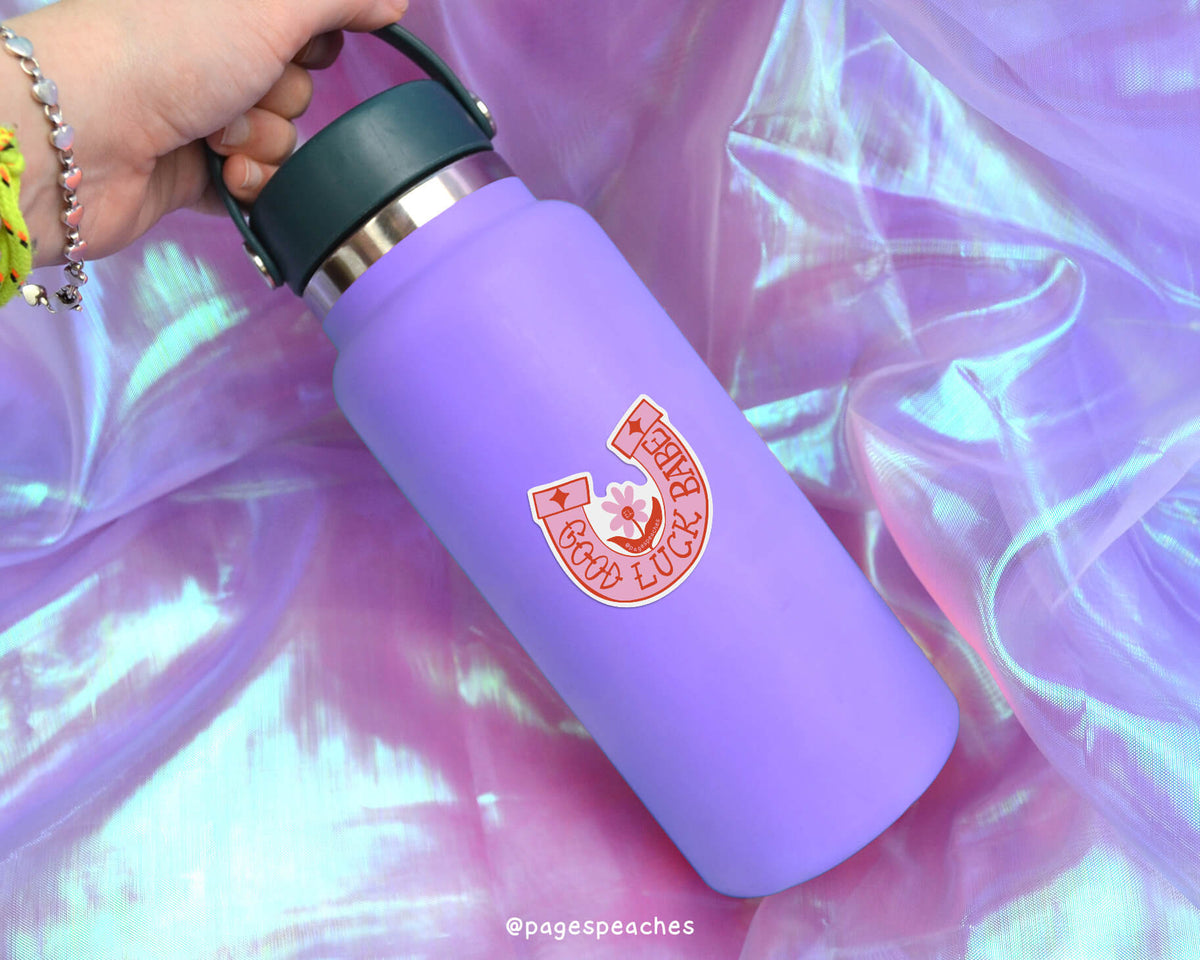 A purple water bottle with a red and white logo on it, held in a hand against a purple fabric background.