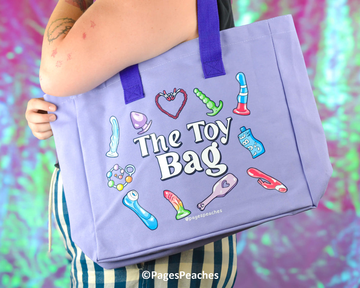 Purple tote bag with colorful illustrations and 'The Toy Bag' text, held by a person against a multicolored background.