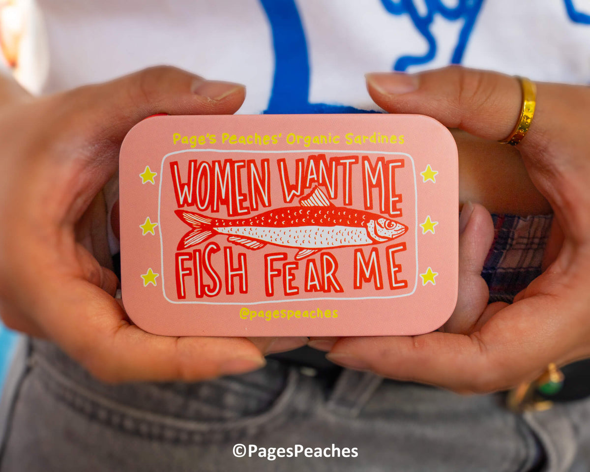 A person is holding a pink tin can with a fish and the text "Women Want Me Fish Fear Me" printed on it.