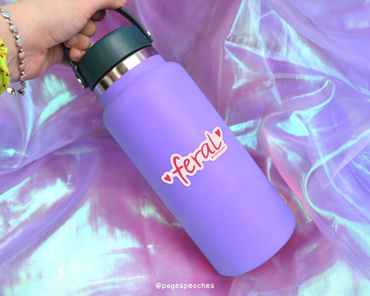 A purple water bottle with a green lid is being held by a person's hand, with a pink and red sticker on the bottle that says 'feral'.