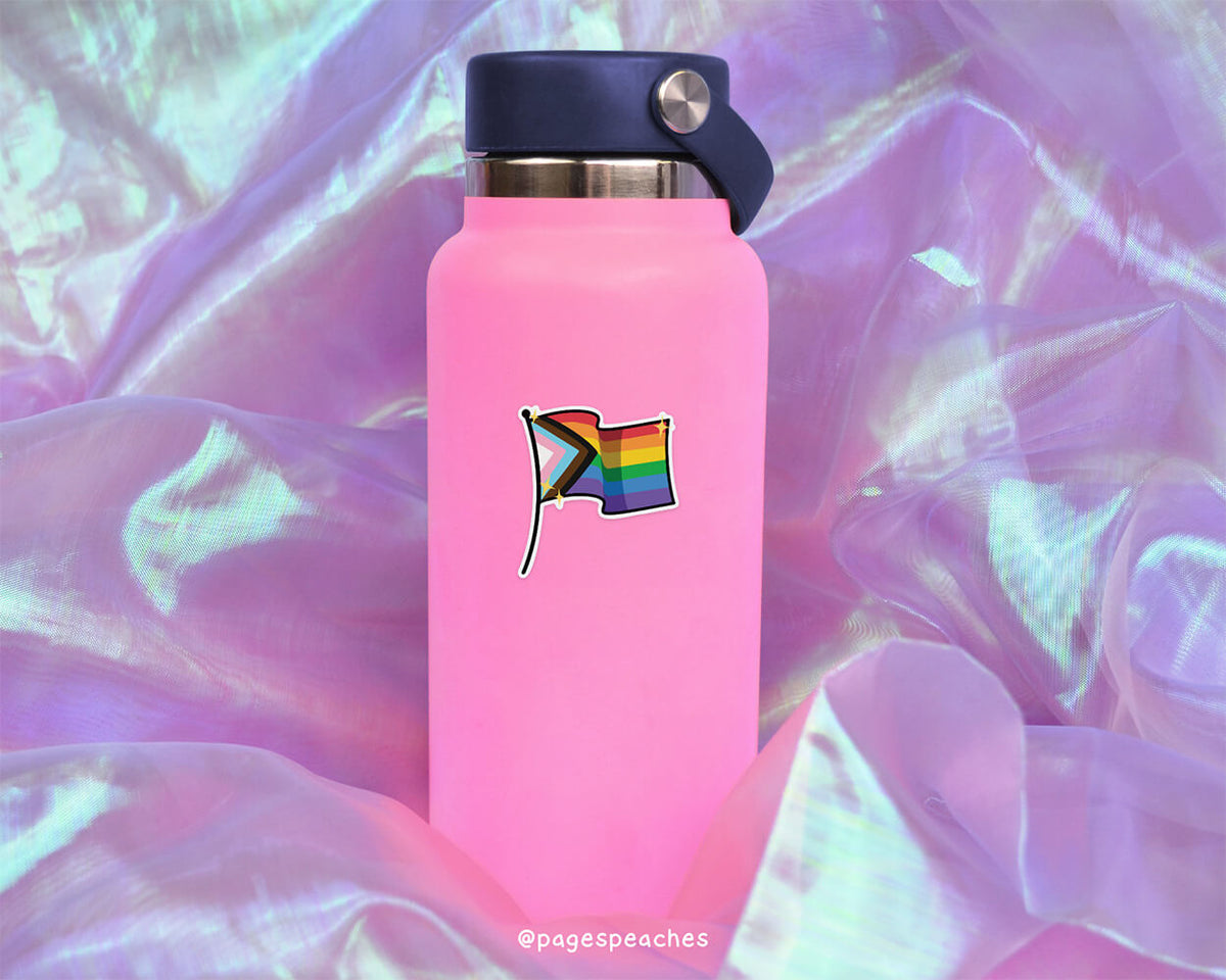 A pink water bottle with a rainbow flag sticker on it, placed on a purple fabric background.